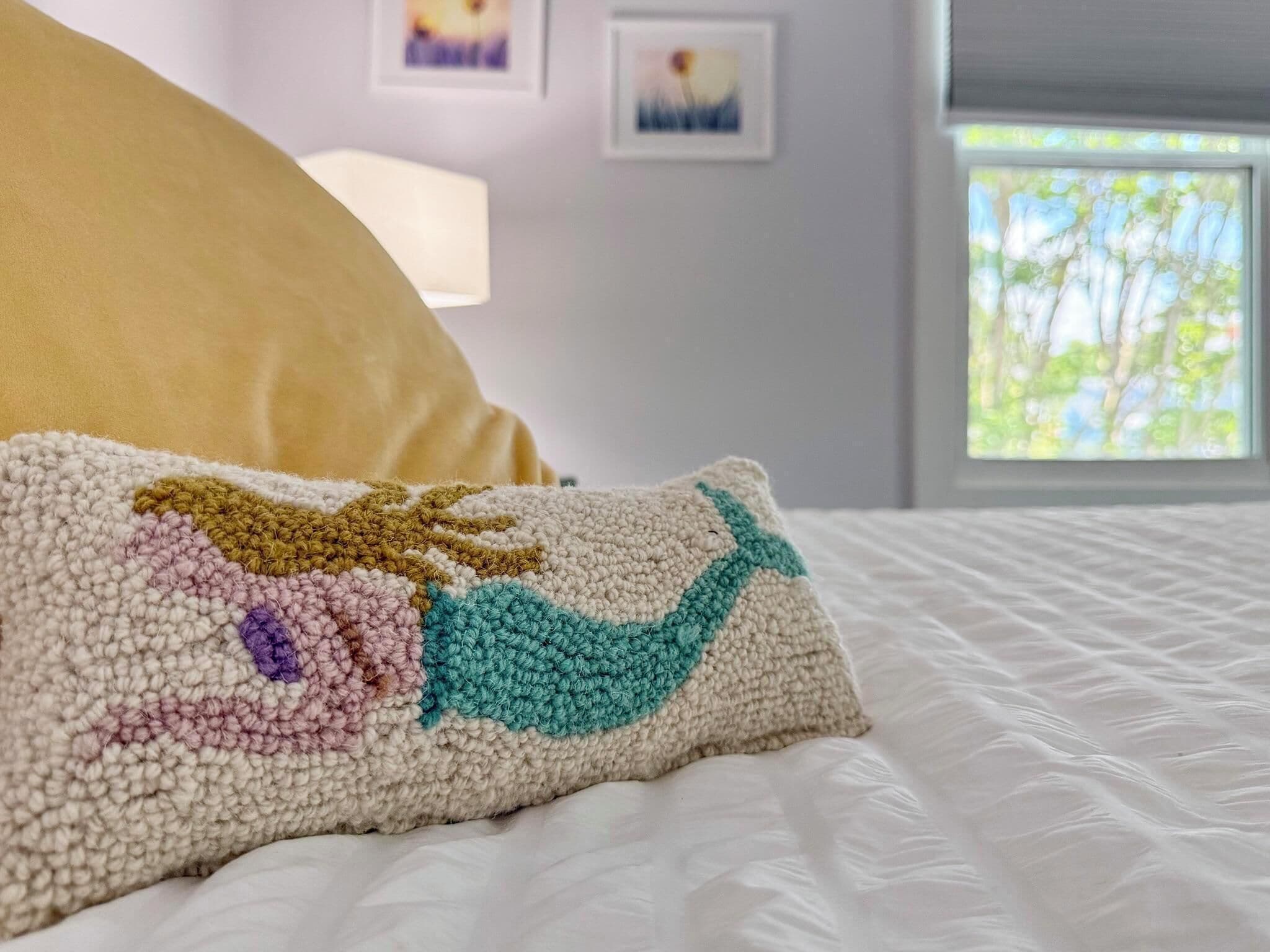 Un lit recouvert d’une couverture blanche  à texture, un coussin tricoté multicolore et un coussin jaune.