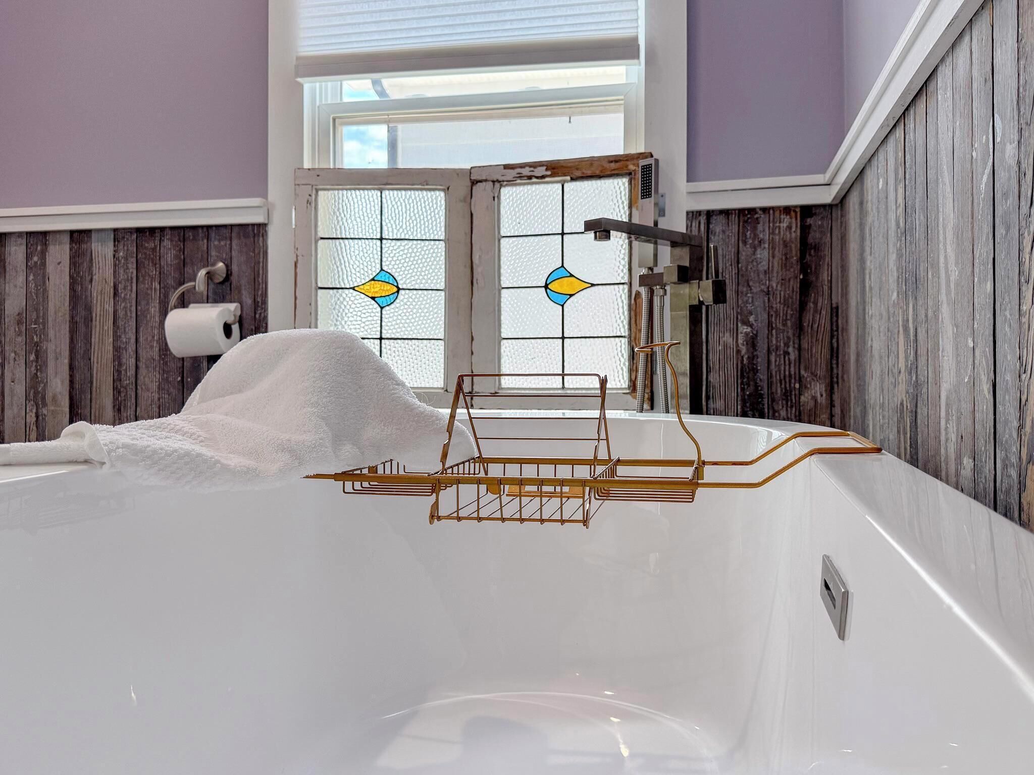 Une salle de bain avec une baignoire, une serviette, une douche et une fenêtre ornée de vitraux.