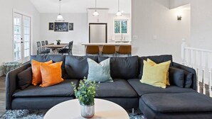 Un salon moderne avec un canapé foncé, une table basse et un coin repas à l’arrière-plan.