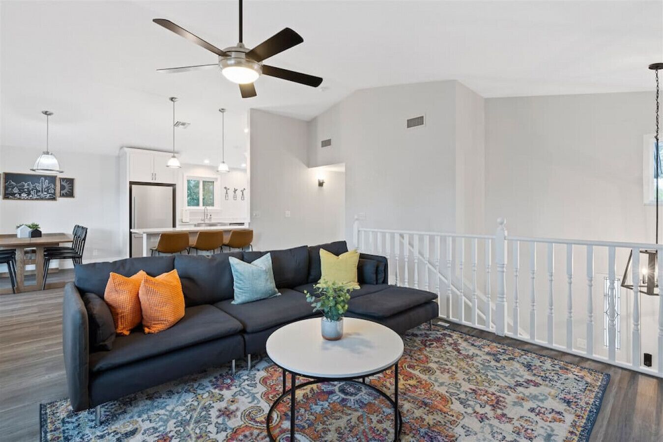 A modern living room with a black sofa, colorful cushions, a white coffee table, and a patterned rug.