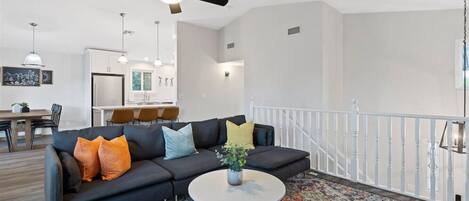 A modern living room with a black sofa, colorful cushions, a white coffee table, and a patterned rug.