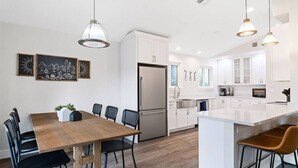 Une cuisine moderne avec des armoires blanches, un réfrigérateur en acier inoxydable et des luminaires suspendus.