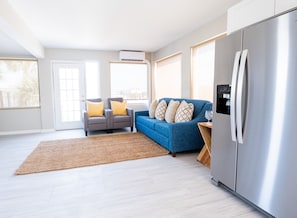 A modern kitchen with a stainless steel refrigerator, a blue sofa with patterned cushions, and a grey armchair with yellow cushions. - 300 Tenth (Myrtle Beach)