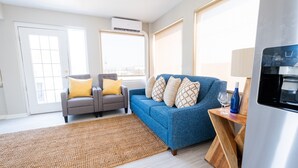A modern living room with a blue sofa, a grey armchair, and a wooden coffee table. - 300 Tenth (Myrtle Beach)