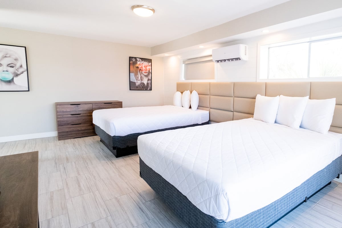 A hotel room with two beds, a wooden headboard, a large window, and an air conditioning unit.