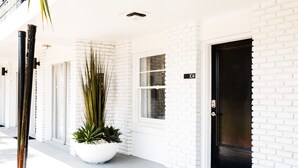 A white brick building with a black door, a potted plant, and a window. - 300 Tenth (Myrtle Beach)
