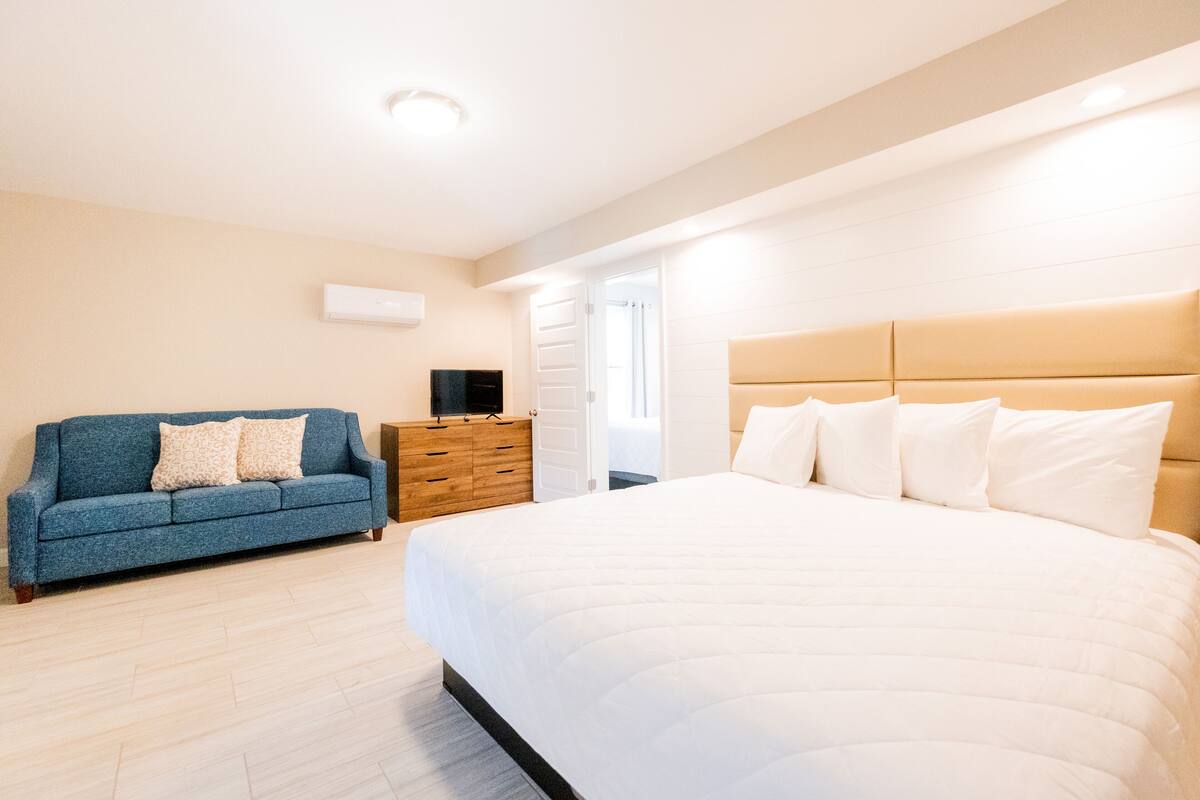 A bedroom with a large bed, a blue sofa, and a wooden dresser.