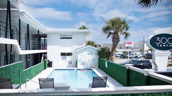 Un hotel moderno con área de piscina, incluyendo un puesto de salvavidas y un letrero que indica la disponibilidad de estacionamiento.
