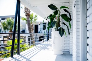 Un balcon agrémenté d’un jardinier blanc, de palmiers et d’un mur en briques blanches.