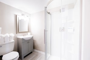 A modern bathroom with a toilet, vanity, and glass shower enclosure. - 300 Tenth (Myrtle Beach)