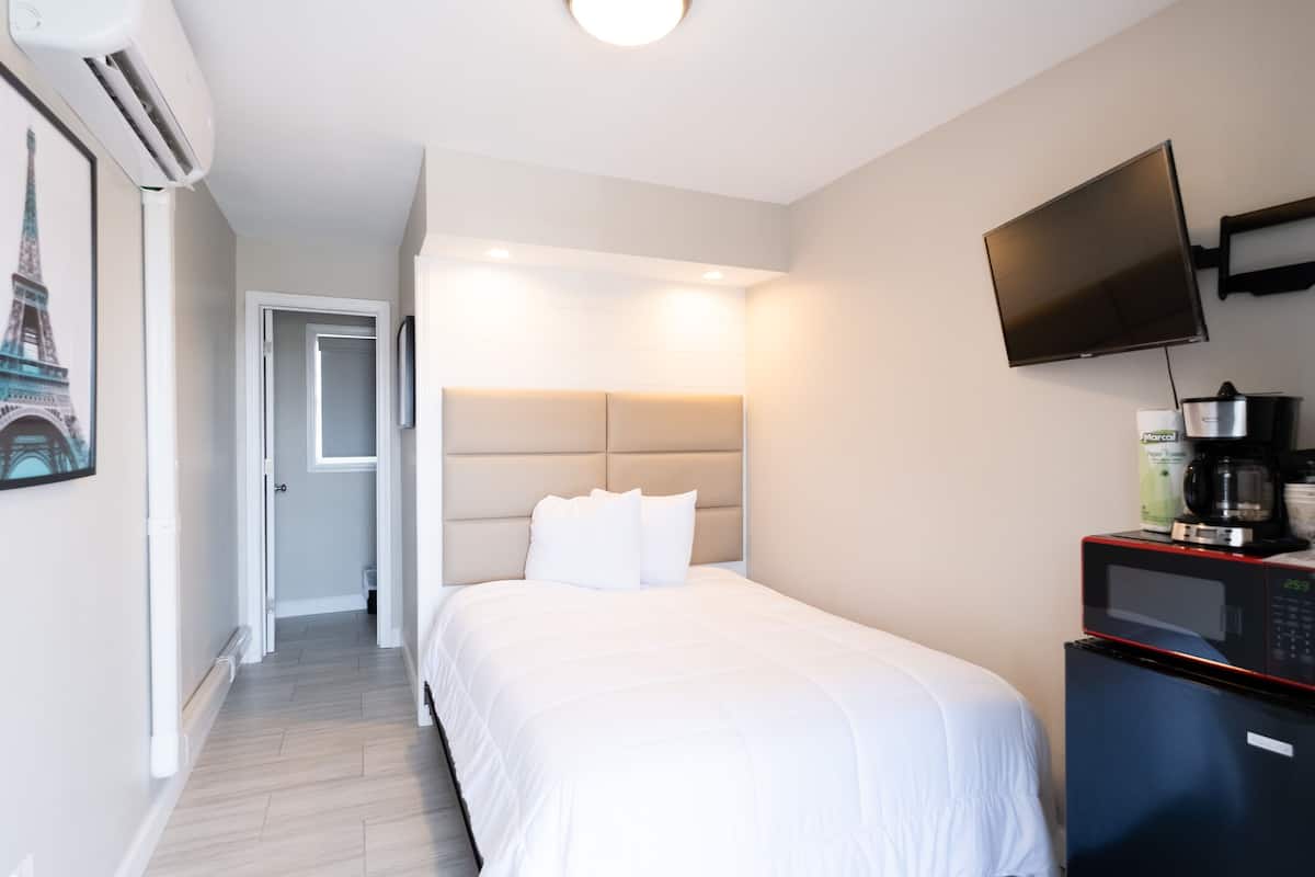 A hotel room with a bed, a flat-screen TV mounted on the wall, a coffee maker, and a framed picture of the Eiffel Tower.