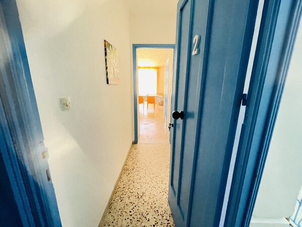 A hallway with a blue door, a light switch, and a textured floor.