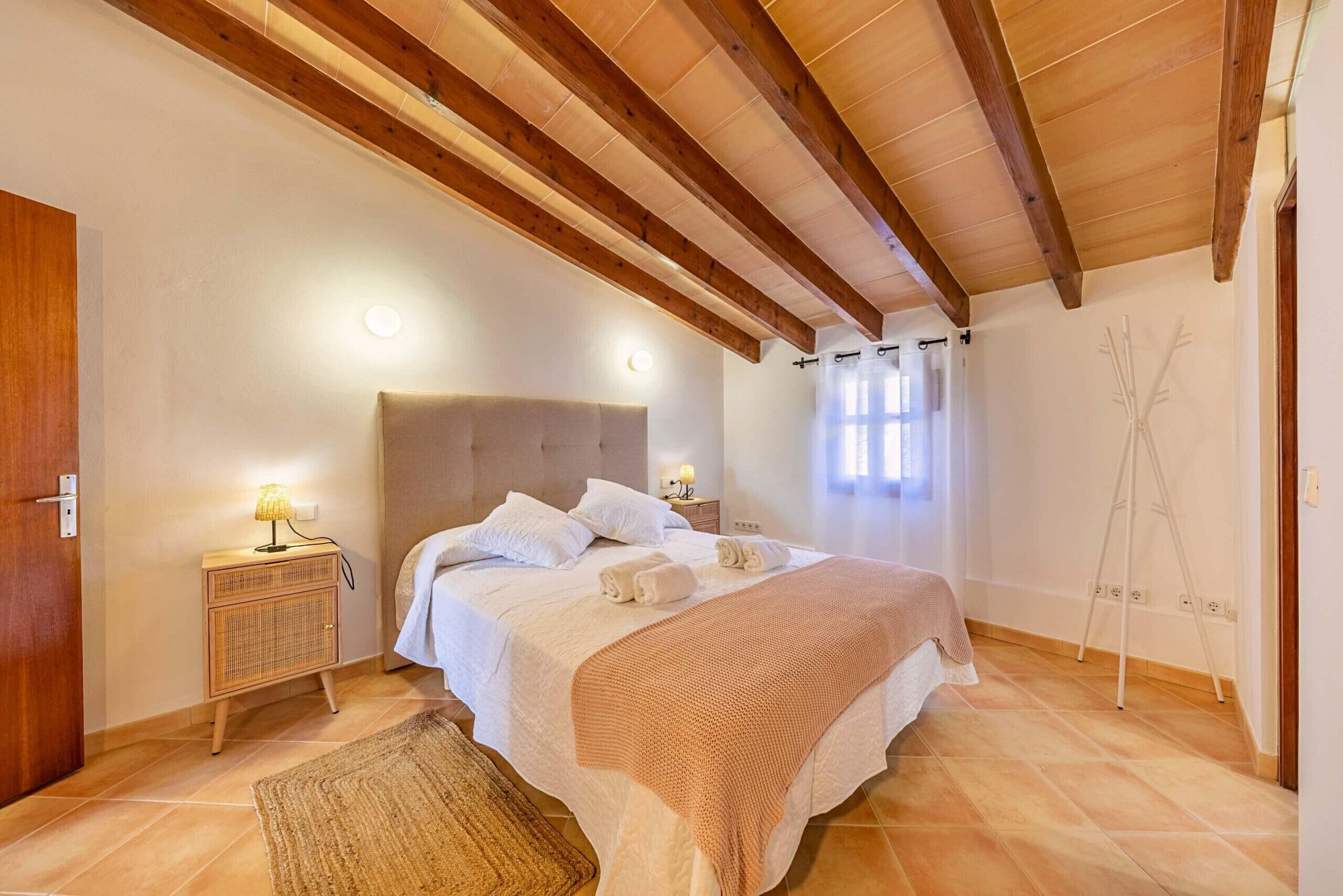 Une chambre avec un plafond en bois, un lit avec une literie blanche, une table de chevet avec une lampe et un lampadaire mural.
