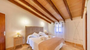 Una camera da letto con soffitto in legno, un letto con lenzuola bianche, un comodino con una lampada e una lampada da terra appesa al muro.