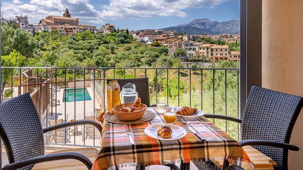 Un balcone con sedie in vimini, un tavolo con cibi per la colazione e vista su una città e montagne.