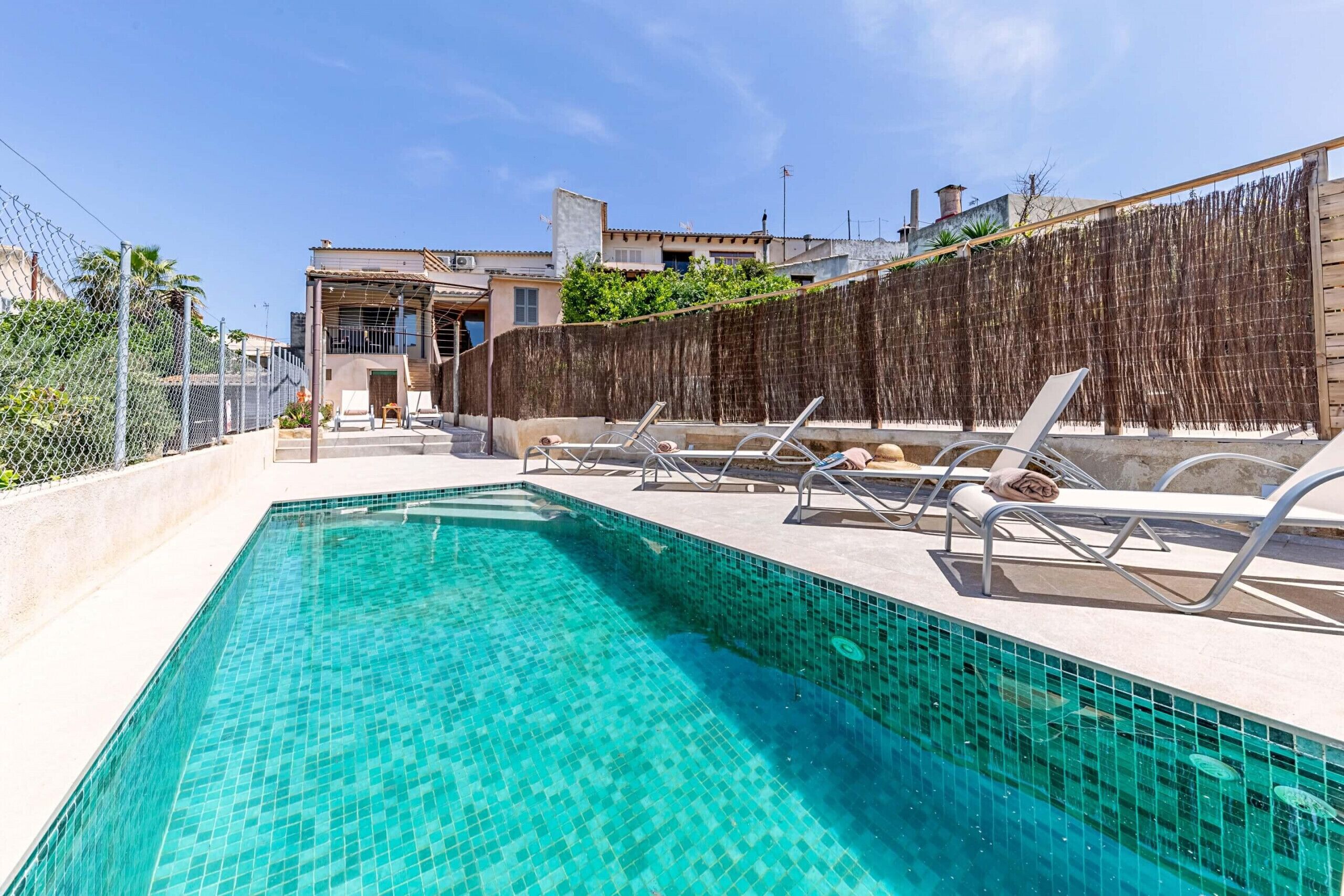 Une piscine à l’eau d’un bleu cristallin, entourée de chaises longues et d’une clôture en bois.