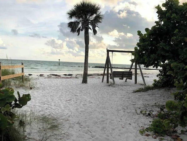A beach with a wooden swing set and a palm tree.
