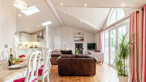 Un vaste espace de vie doté d’un plancher en bois, d’un canapé en cuir marron, d’une table à manger blanche avec des chaises, et d’un téléviseur placé à l’arrière-plan.