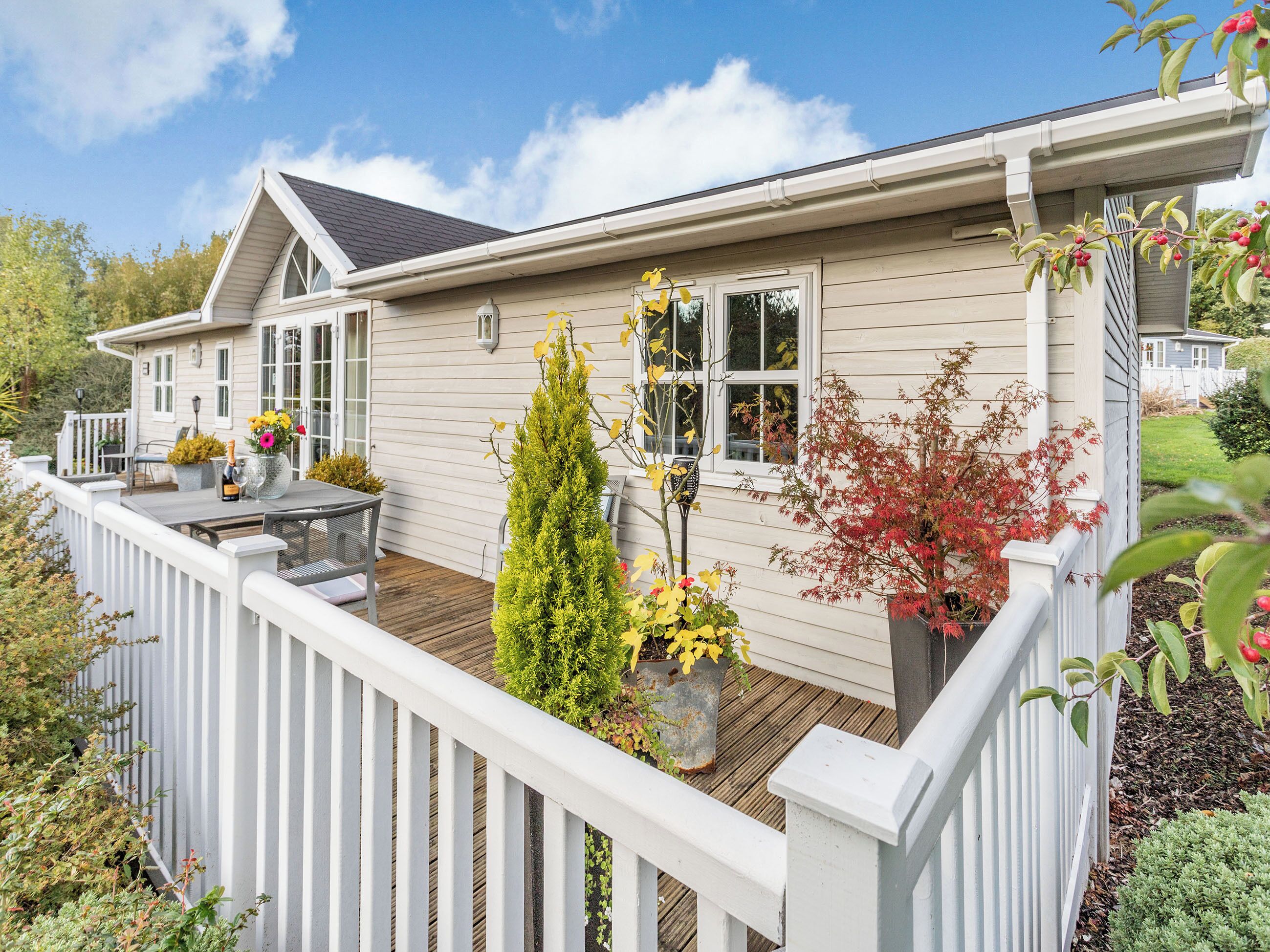 Een huis met een houten terras, witte leuningen en diverse potplanten.