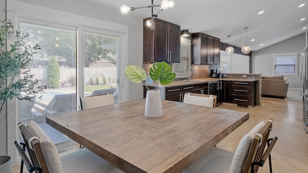 A modern kitchen with dark wooden cabinets, a central island, and a dining area with a wooden table and chairs. - Private Pool, Hottub, Steamshower just 10 minutes from Grand Rapids (Grandville)