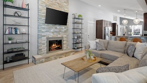 A modern living room with a fireplace, built-in shelves, a sofa, and a kitchen in the background. - Private Pool, Hottub, Steamshower just 10 minutes from Grand Rapids (Grandville)