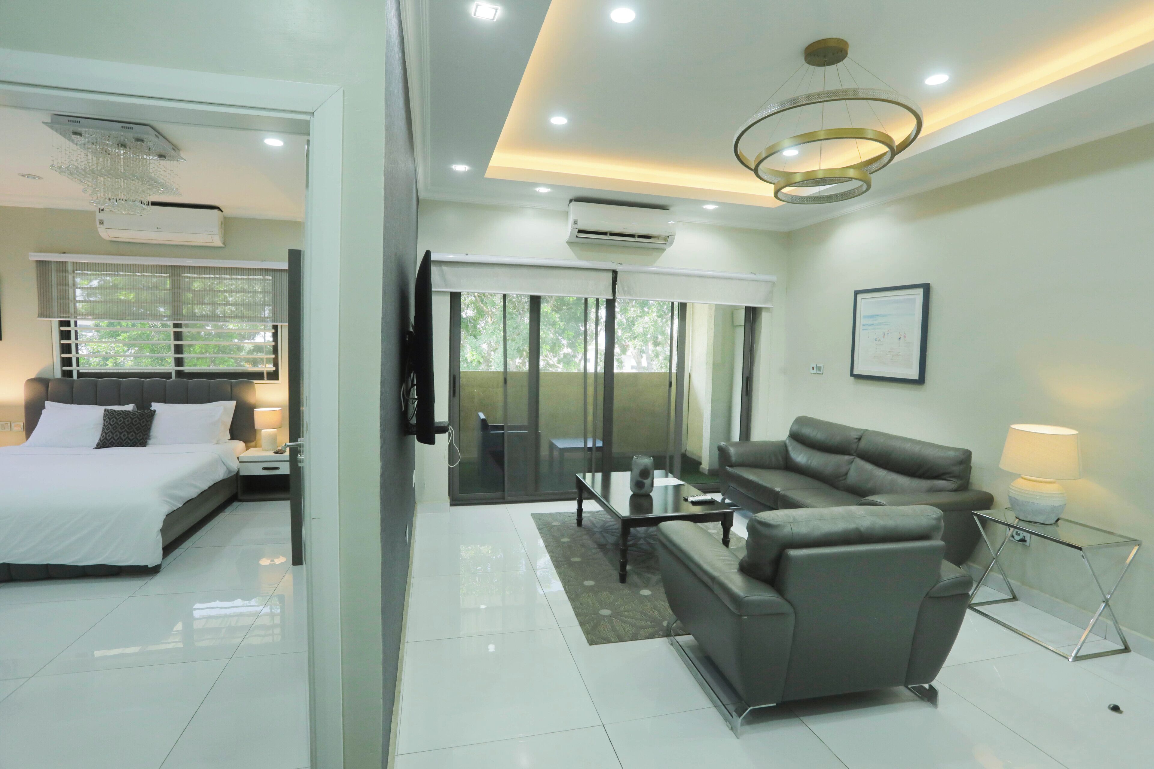 A modern hotel room with a bed, sofa, and a dining area.