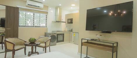Una sala de estar moderna con televisor de pantalla plana, un comedor con sillas, una cocina equipada y un amplio ventanal.