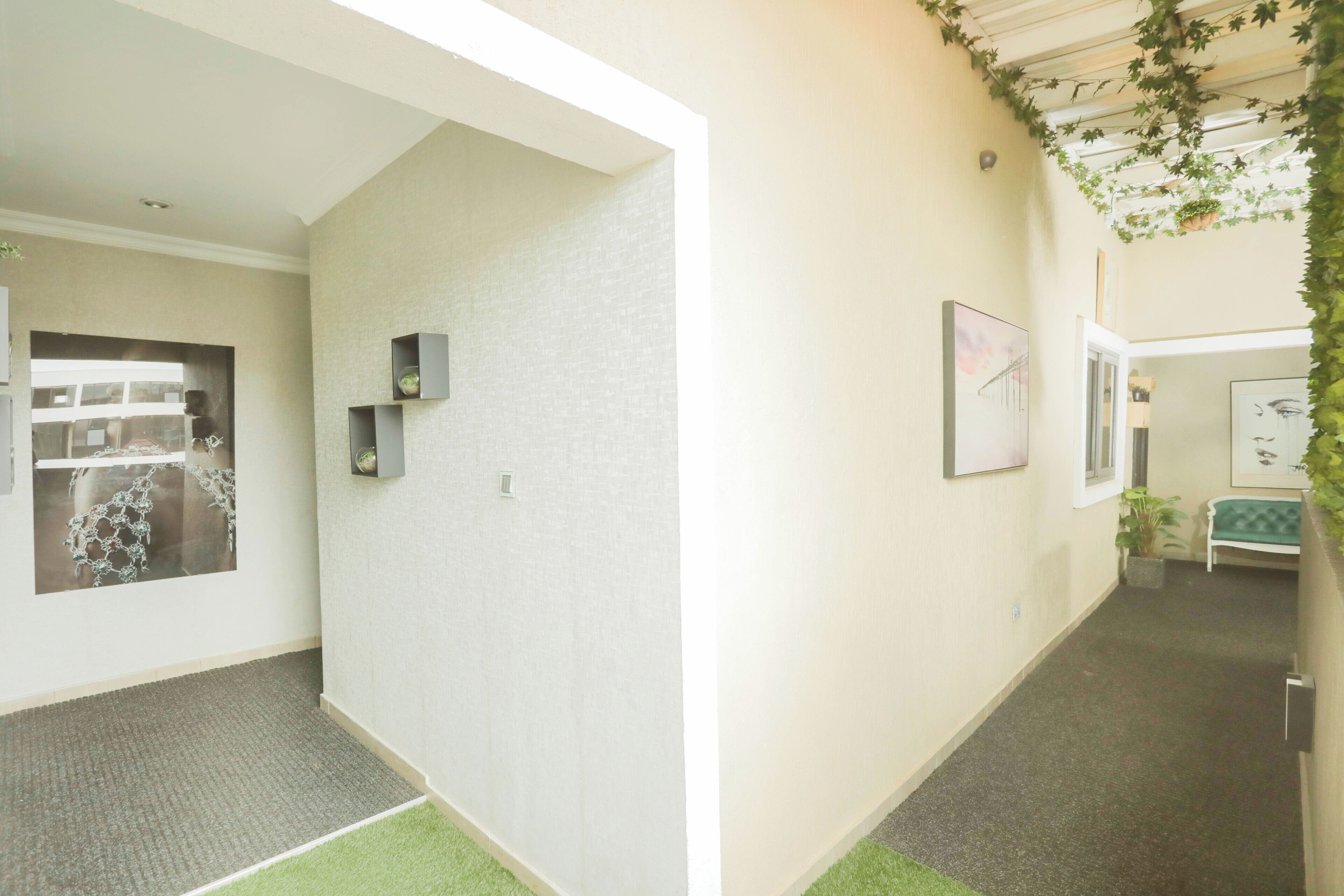 A hallway with a green carpet, a white wall with a picture frame, and a door leading to a room with a green couch.