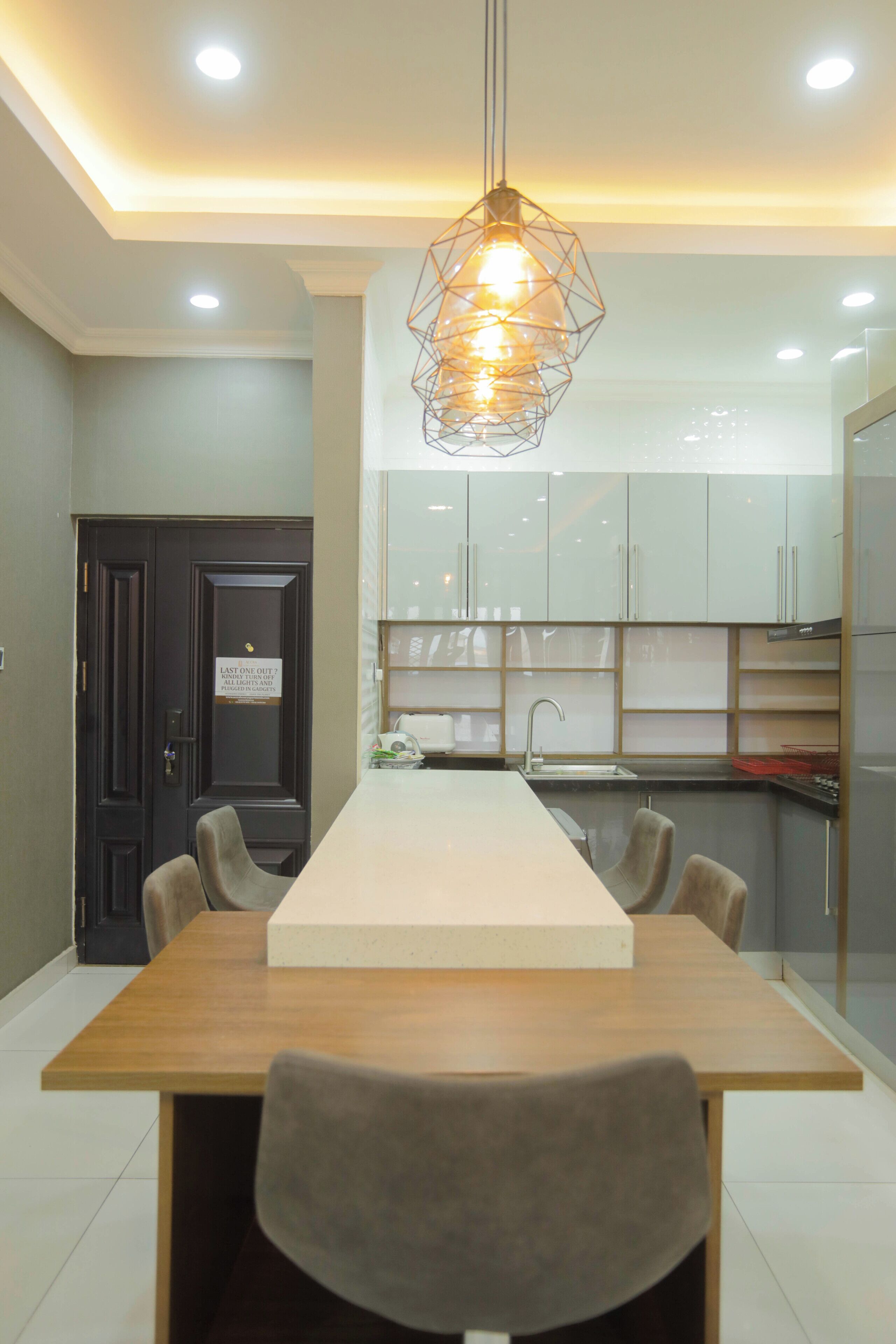 A modern kitchen with white cabinets, a wooden dining table, and a unique geometric pendant light.