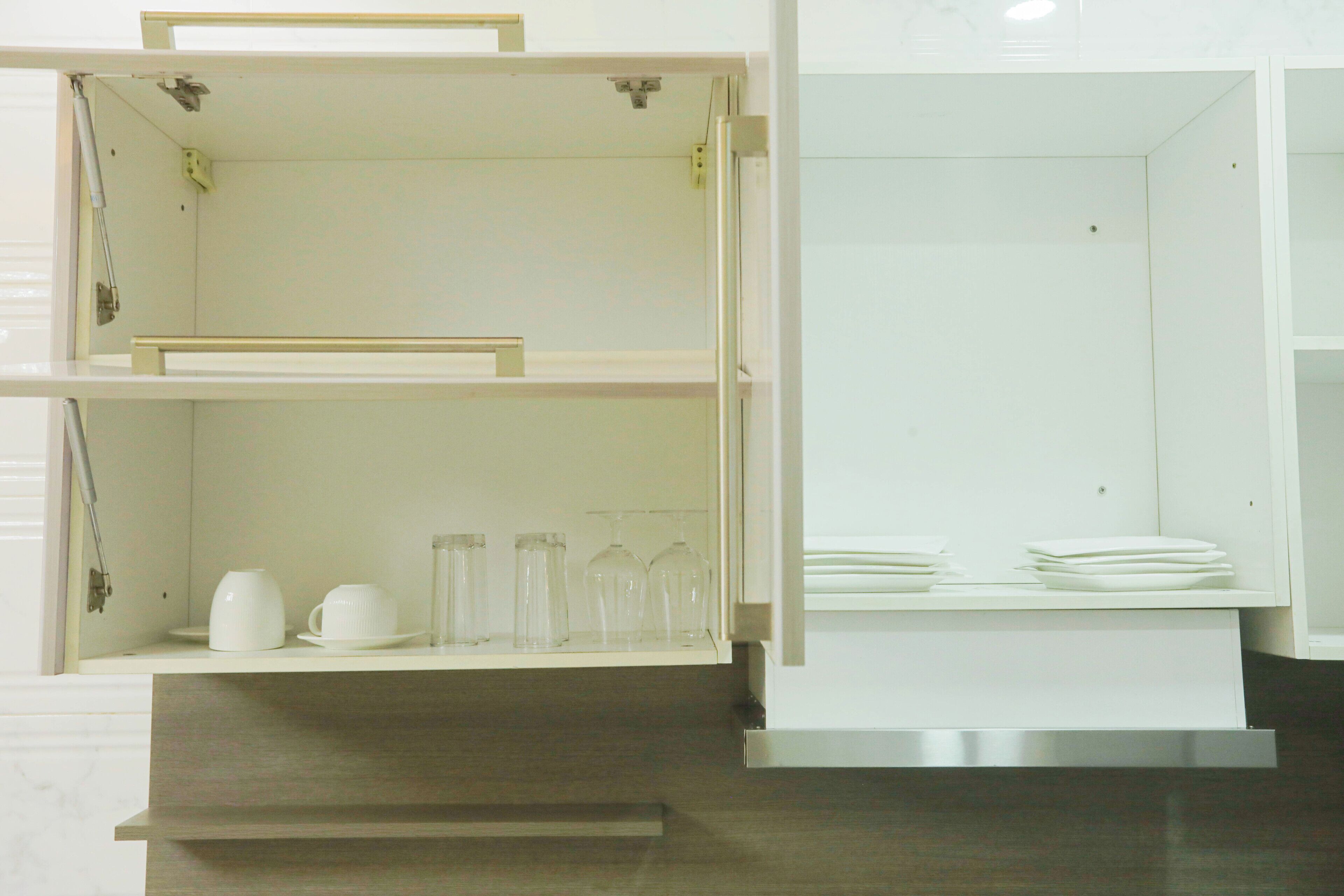 A kitchen with white cabinets, a stainless steel range hood, and a countertop with glassware and plates.