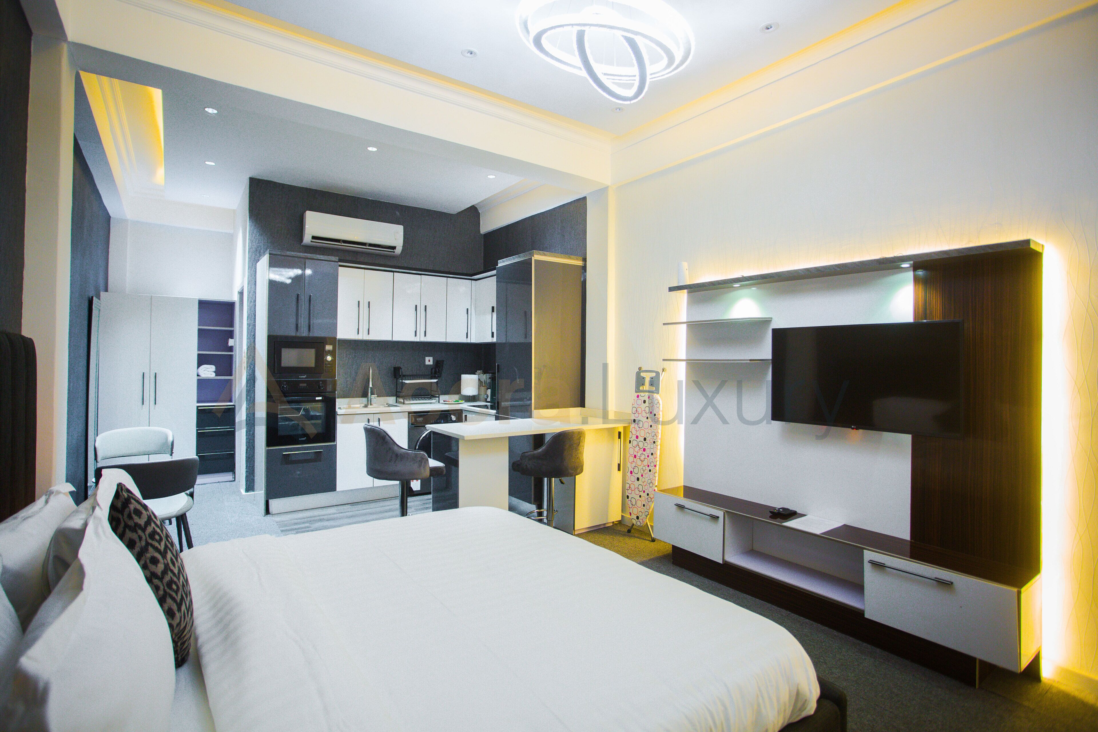 A modern hotel room with a bed, a desk, a chair, a TV, and a kitchenette.