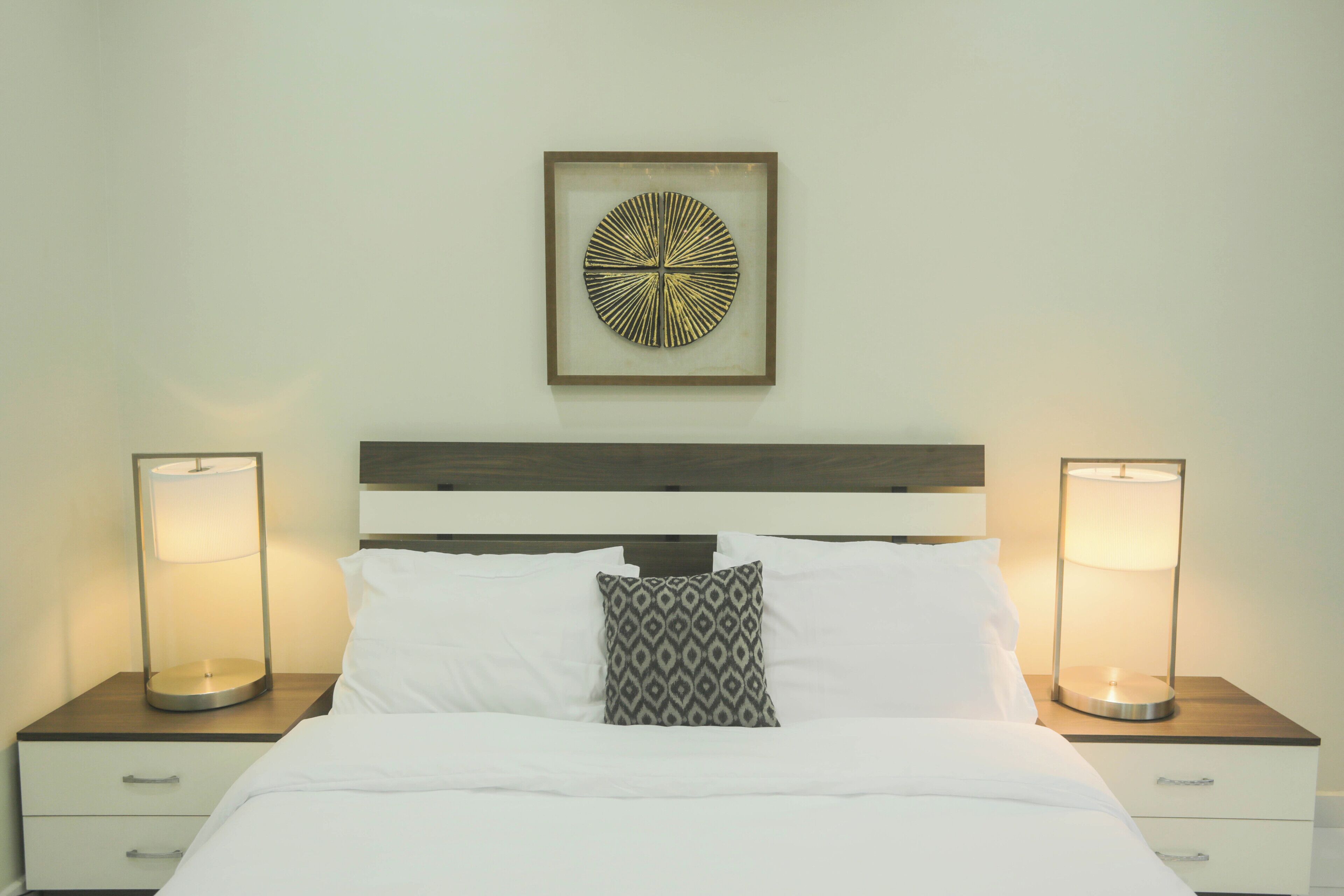 A neatly made bed with white linens, a patterned pillow, and two bedside lamps on wooden nightstands.