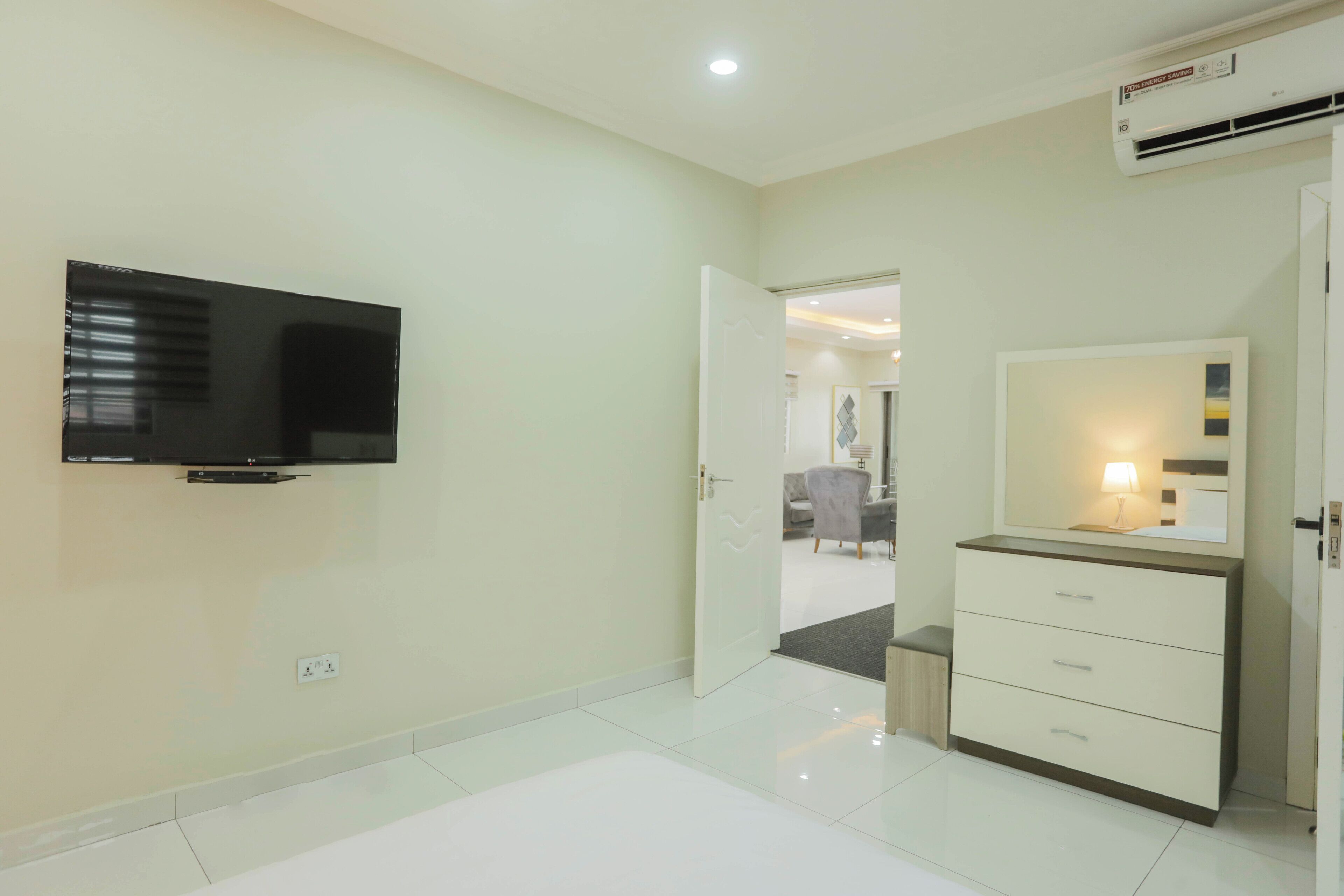 A modern hotel room with a flat-screen TV mounted on the wall, a bedside table with a lamp, and a wardrobe.