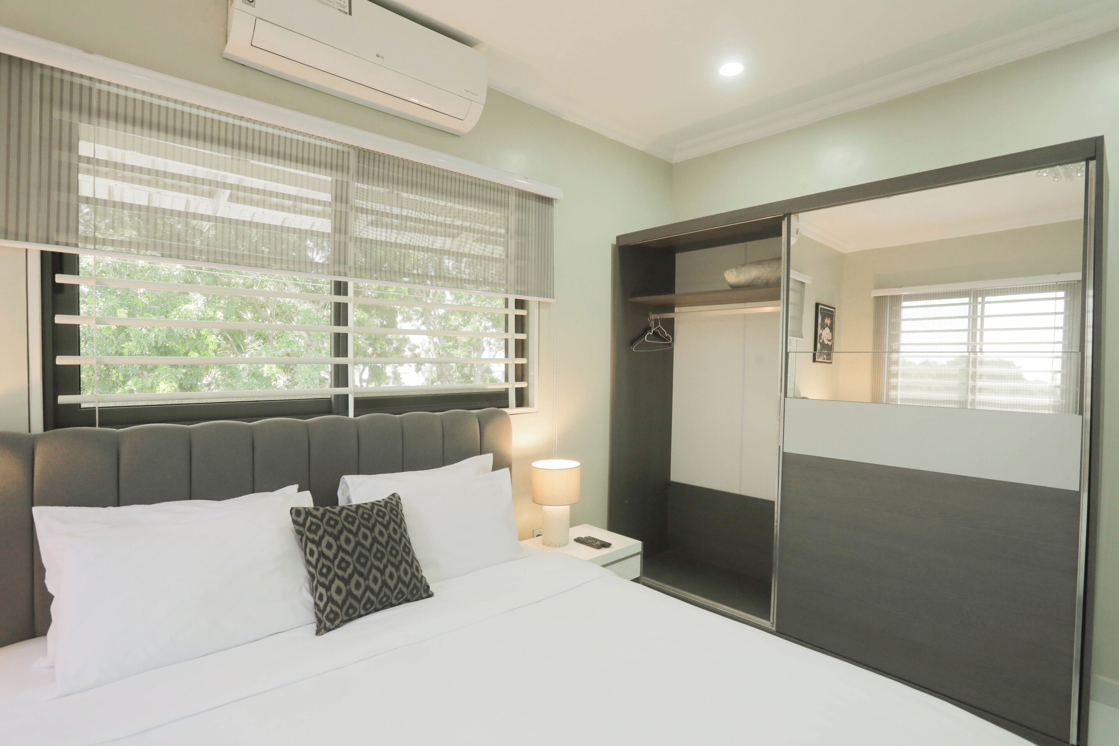 Une chambre moderne avec un grand lit, une lampe de chevet, une armoire et une fenêtre avec des stores.
