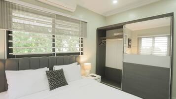 A modern bedroom with a large bed, a bedside lamp, a wardrobe, and a window with blinds.