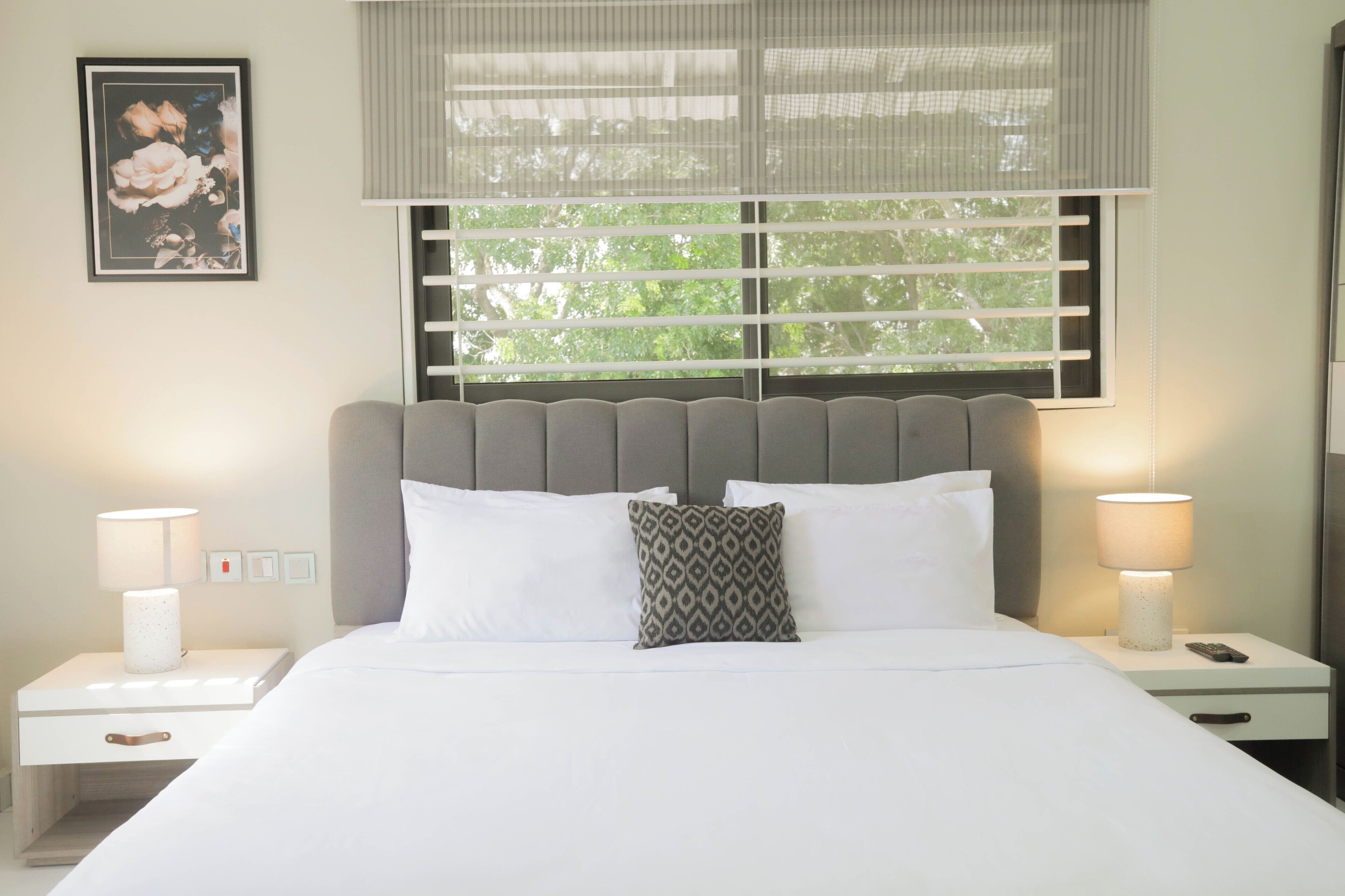 A neatly made bed with white linens, a grey headboard, and two bedside lamps.