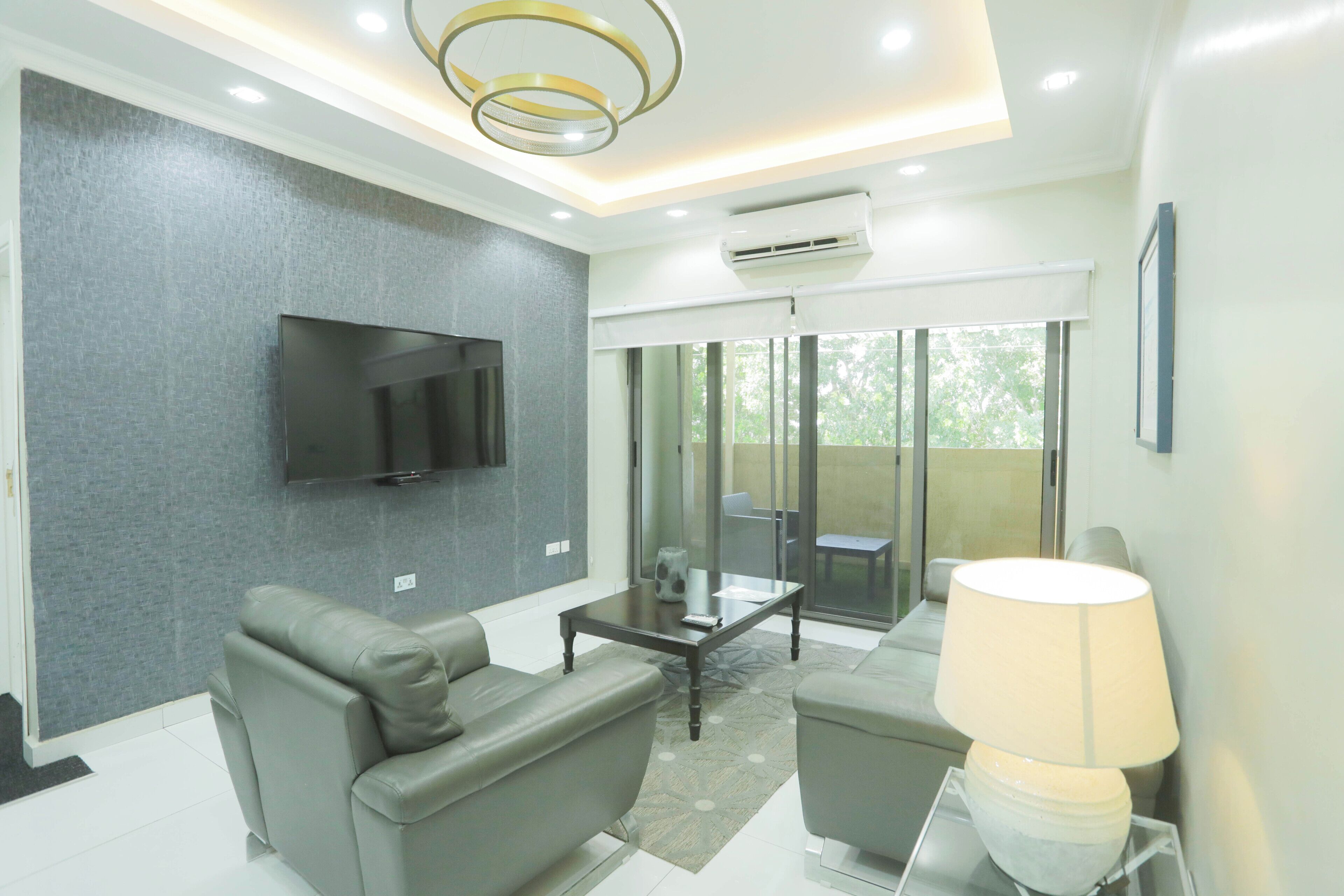 A modern living room with a flat-screen TV, grey sofas, a coffee table, and a lamp.