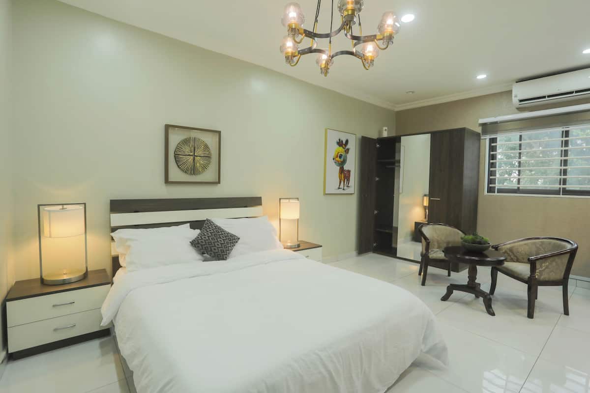 A bedroom with a large bed, bedside lamps, a chandelier, and a small table with chairs.