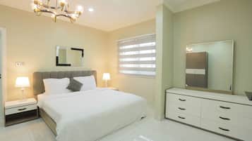 A modern bedroom with a large bed, bedside tables with lamps, a dresser, a mirror, and a chandelier.