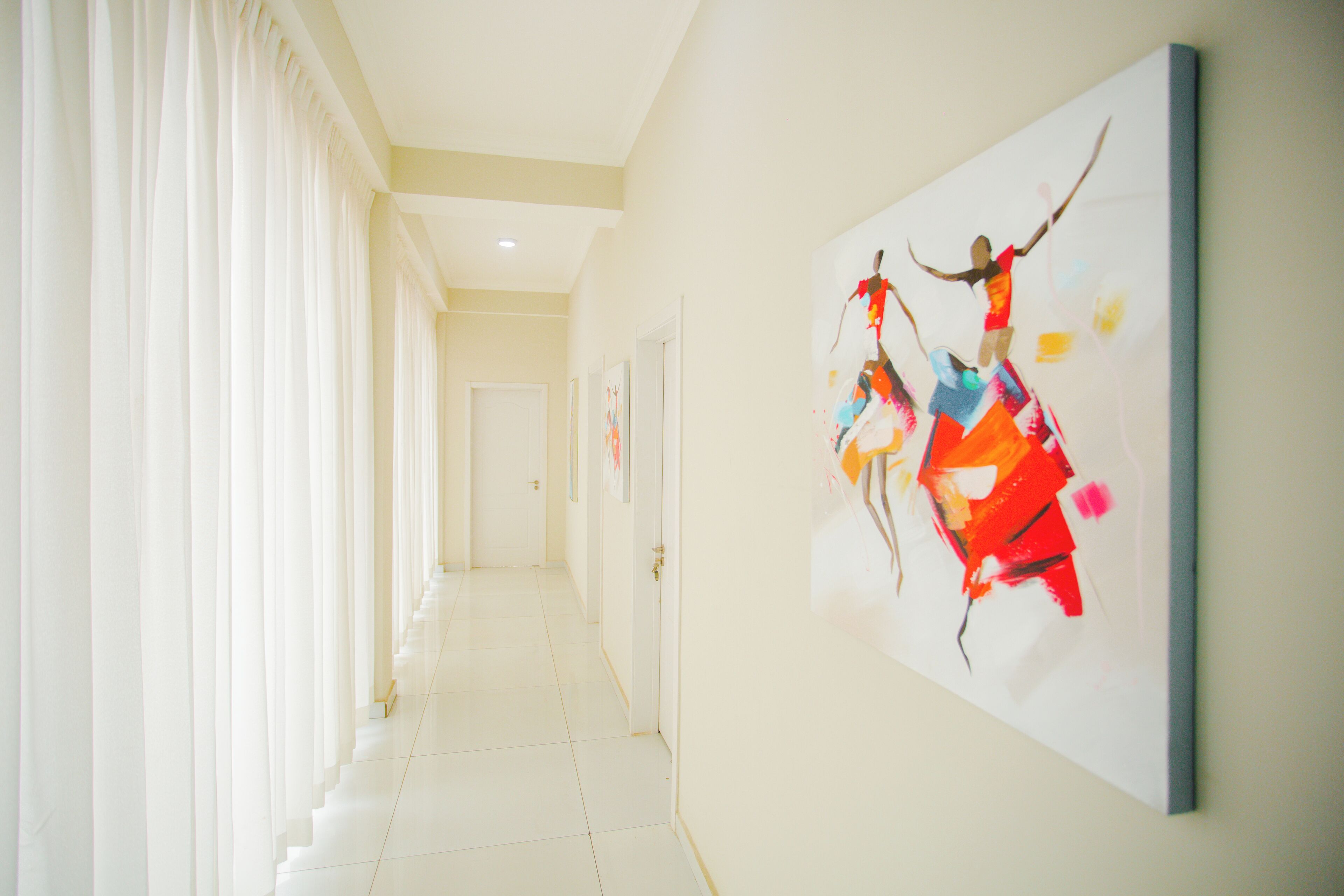 A hallway with a long corridor, a door at the end, and a colorful abstract painting on the wall.