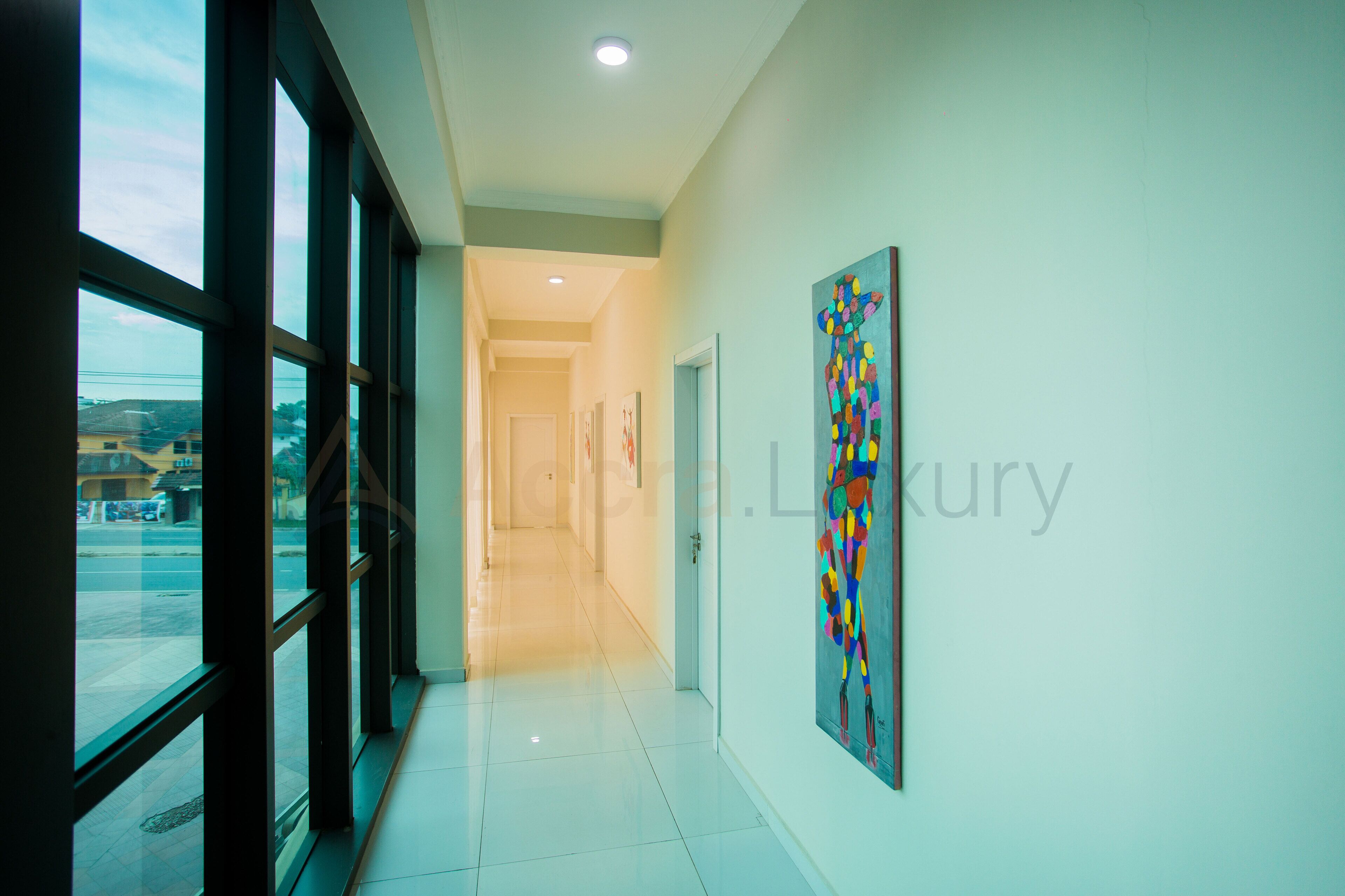 A hallway with large windows, a tiled floor, and a colorful abstract painting on the wall.