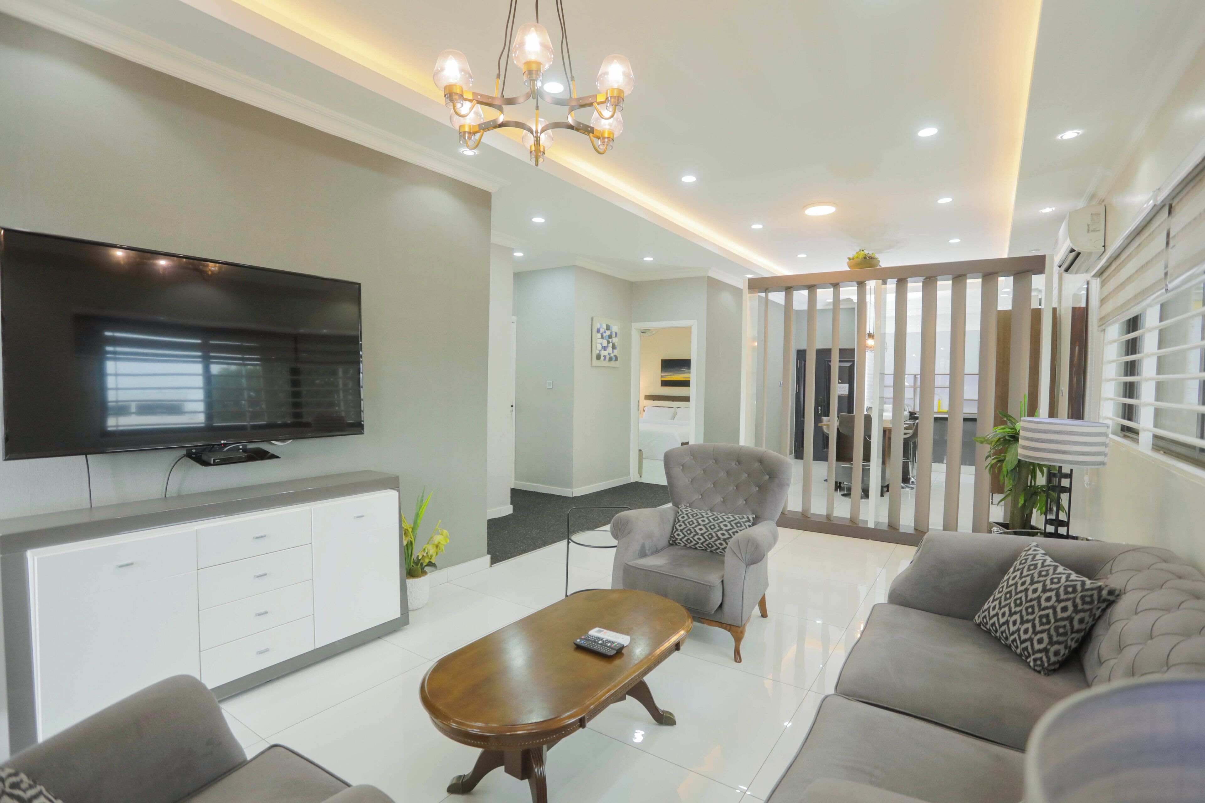 A modern living room with a flat-screen TV, a sofa, a coffee table, and a grey armchair.