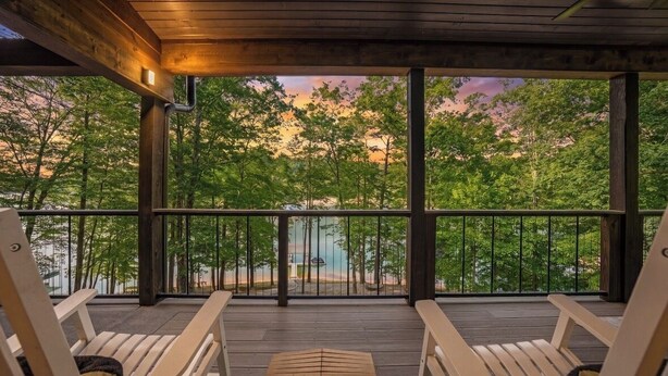 Terraza de madera con dos sillas y una mesa, con vistas a un área boscosa y el agua.