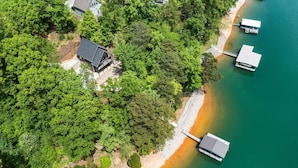 Vista aérea de una propiedad costera con playa, varias embarcaciones amarradas y una casa rodeada de exuberante vegetación.