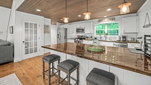 Una cocina con techo de madera, armarios blancos, una isla grande con taburetes e iluminación colgante.