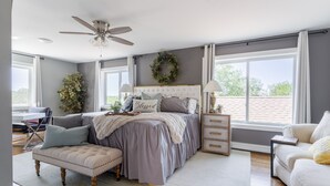 Un dormitorio con cama, ventilador de techo, mesita de noche, cómoda y ventana con vistas.