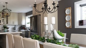 Cocina moderna con comedor, que incluye una araña, velas blancas y un pájaro decorativo.