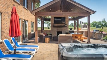 Un espace patio aménagé avec des chaises longues, un jacuzzi, un mur en briques et un téléviseur fixé au mur.