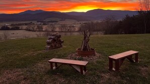Une vue sur le coucher de soleil, avec un banc en bois et un foyer au milieu d’un champ d’herbe.