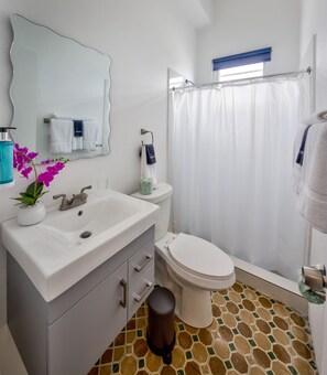 A bathroom with a white sink, toilet, and shower curtain. - Casa Pelayo (San Juan)